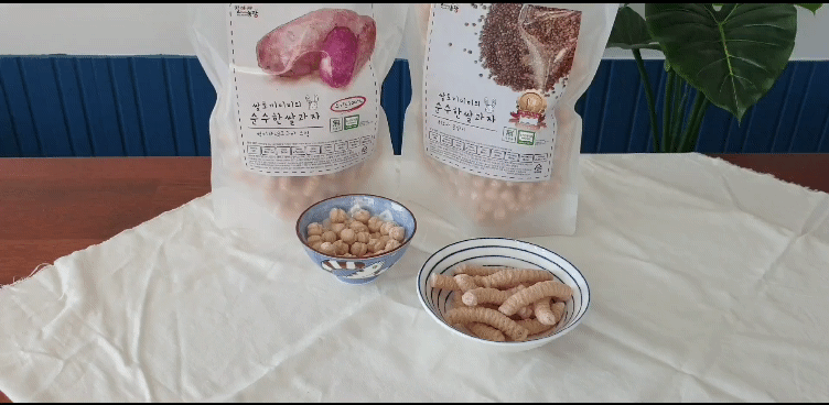 흰색 배경 위에 질마재농장 유기농쌀과자 현미귀리스틱 제품의 패키지와 함께 과자 제품이 부어져 있는 모습.